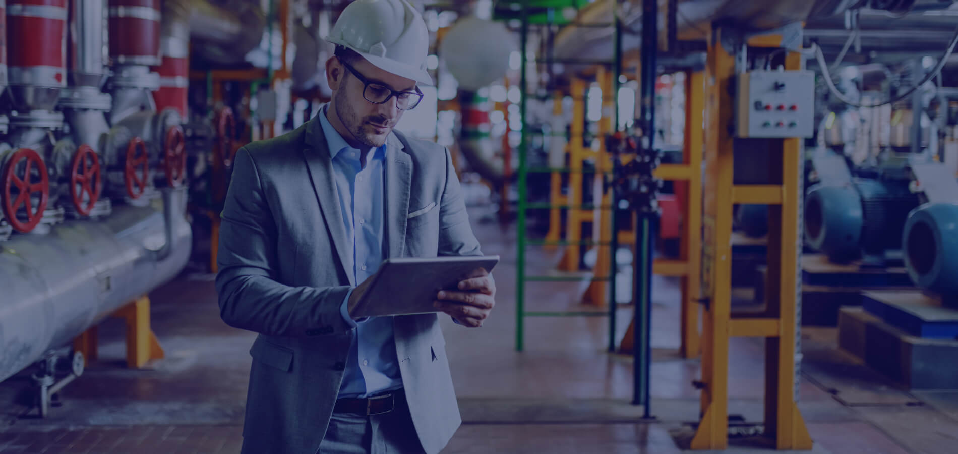 Ingenieur in Schutzhelm und Anzug inspiziert eine industrielle Produktionsanlage mit einem Tablet.